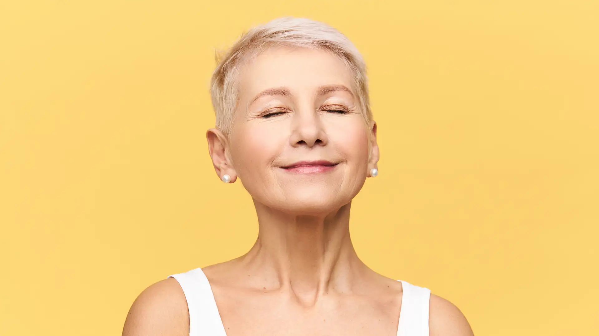 Mature woman with short pixie hair and smooth, radiant skin smiling with eyes closed after rejuvenation treatment in Thornhill clinic