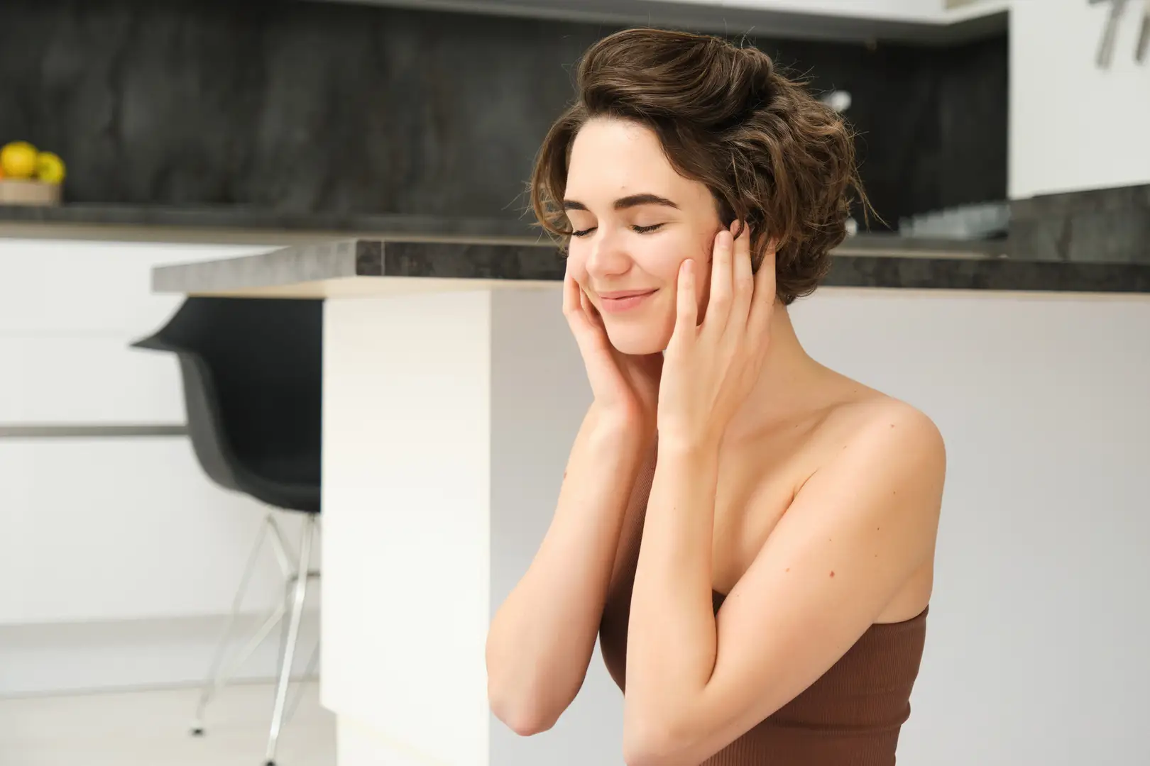 Young woman with hydrated, radiant skin gently touching her face after an anti-aging treatment in Toronto