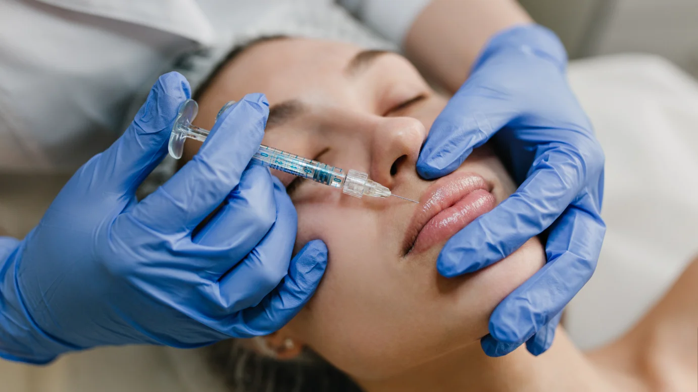 Clinical close-up of a licensed practitioner in blue gloves administering a Botox injection to a patient’s lips