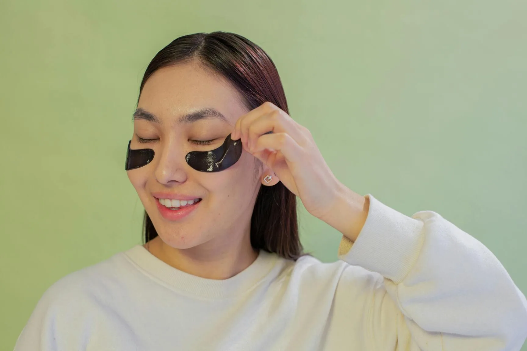 Smiling woman applying under-eye patches for skin hydration and rejuvenation