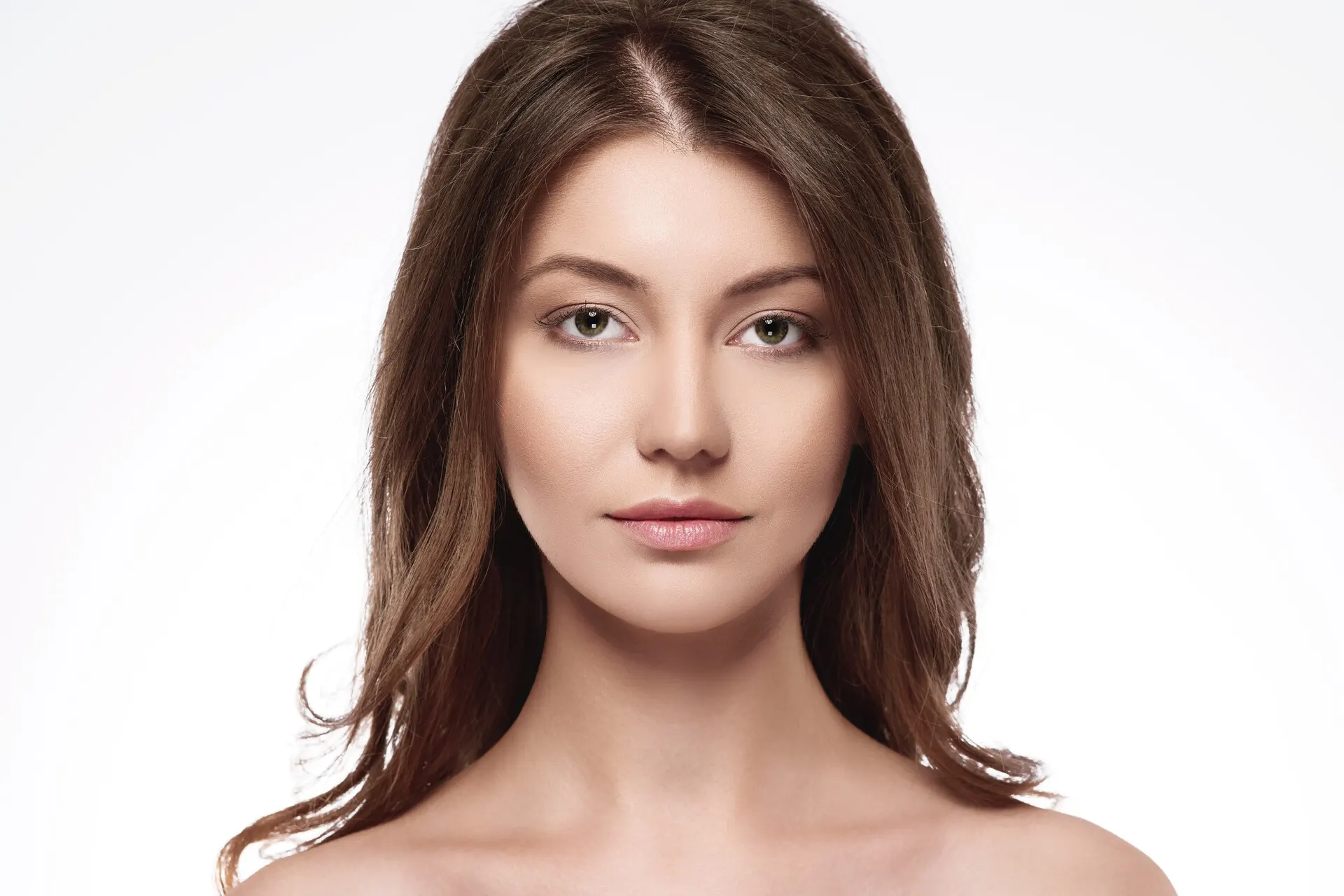 Close-up portrait of a young woman with clear, glowing skin, soft makeup, and natural brown hair against a white background.